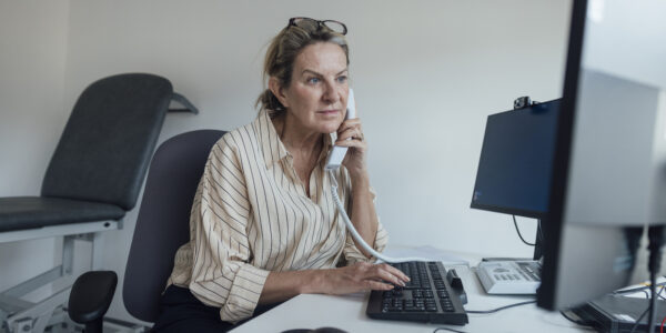 Feature image A healthcare professional (woman) sat at her desk speaking on the phone.